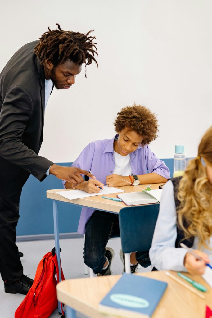 A teacher helps a student with a lesson in a classroom setting.
